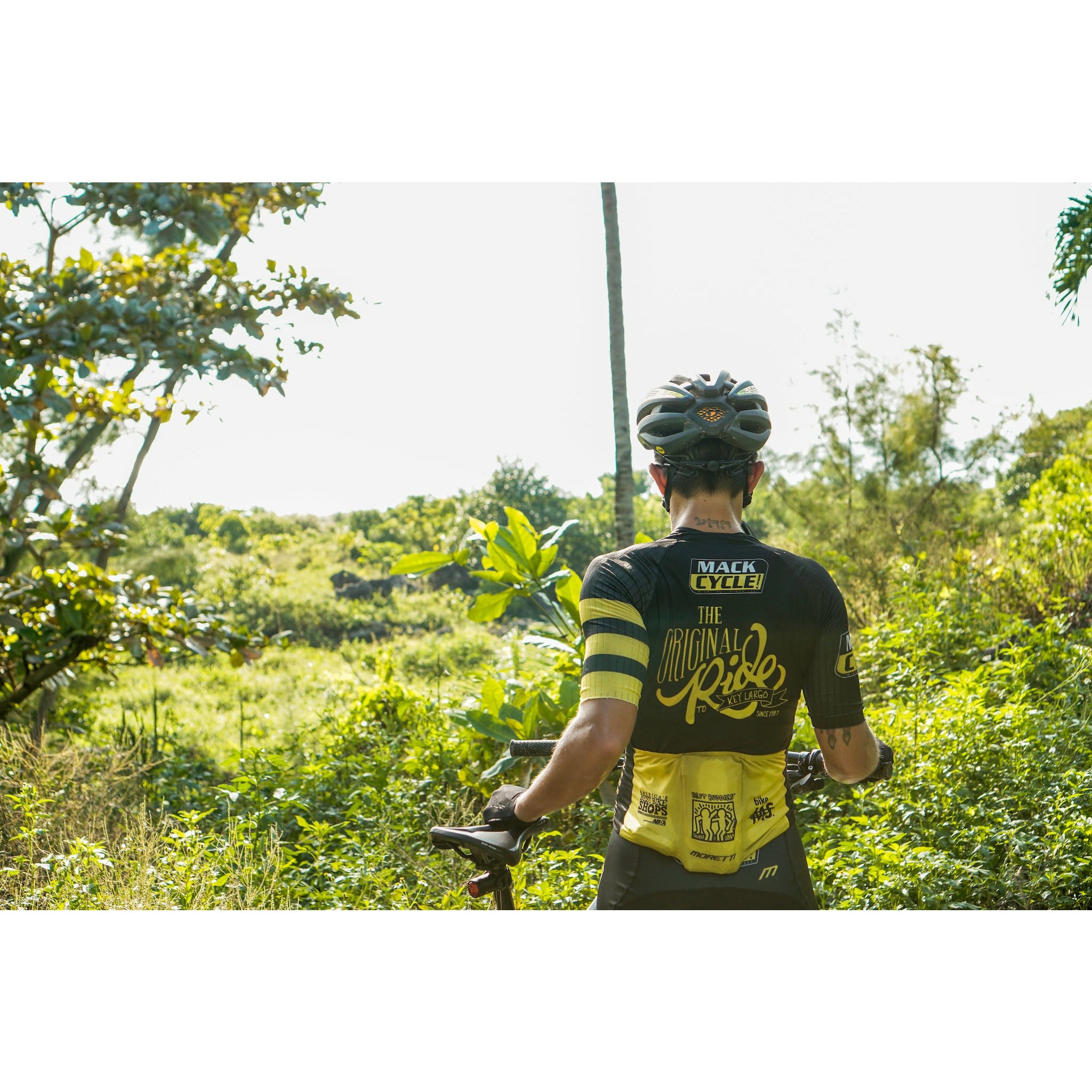 Bavie Grafals looking out over the greenery at the Virginia Key Mountain Bike Trails in Miami. She is wearing her Mack Cycle black and yellow "original ride" cycling kit